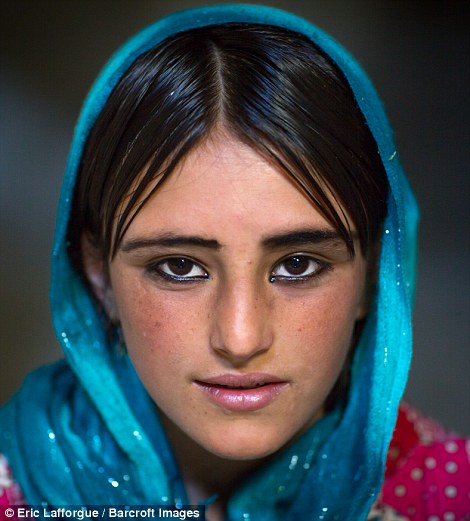 Portrait of an Afghan girl with kohled eyes, wearing a vibrant blue scarf, traditional of the brightly coloured clothing