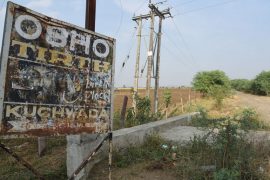 A rusty signboard featuring Osho on the main road leading to the village